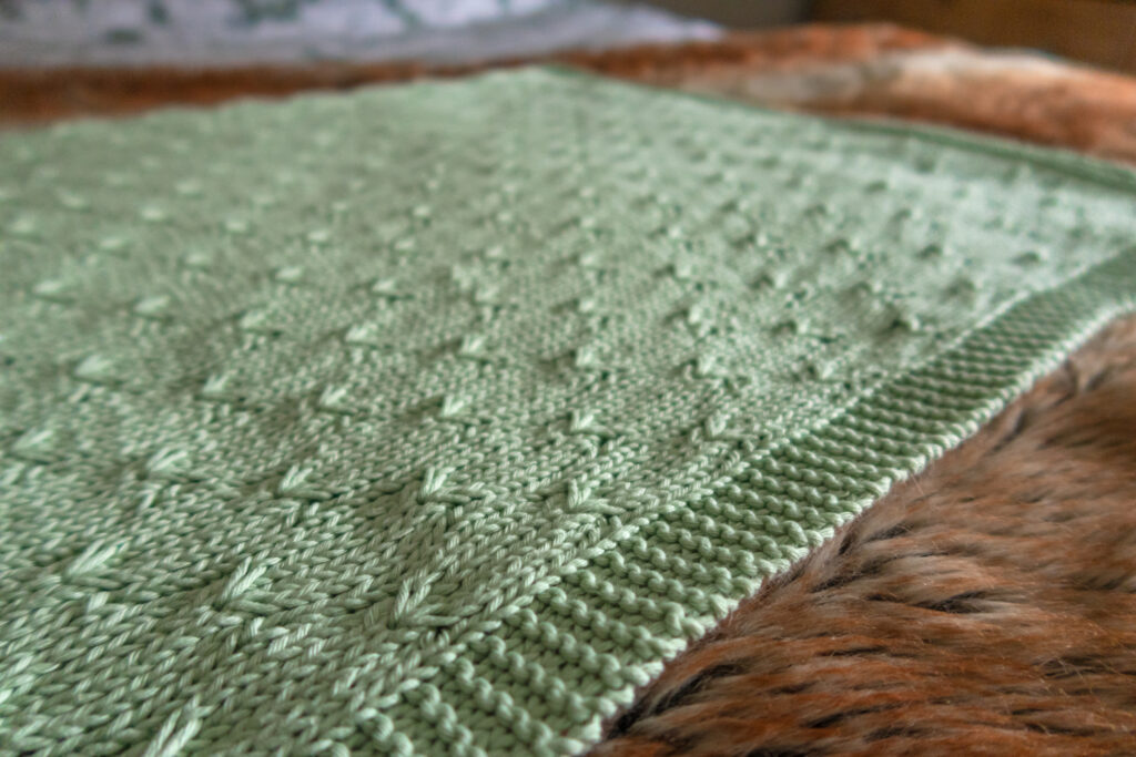A green knitted baby blanket pattern