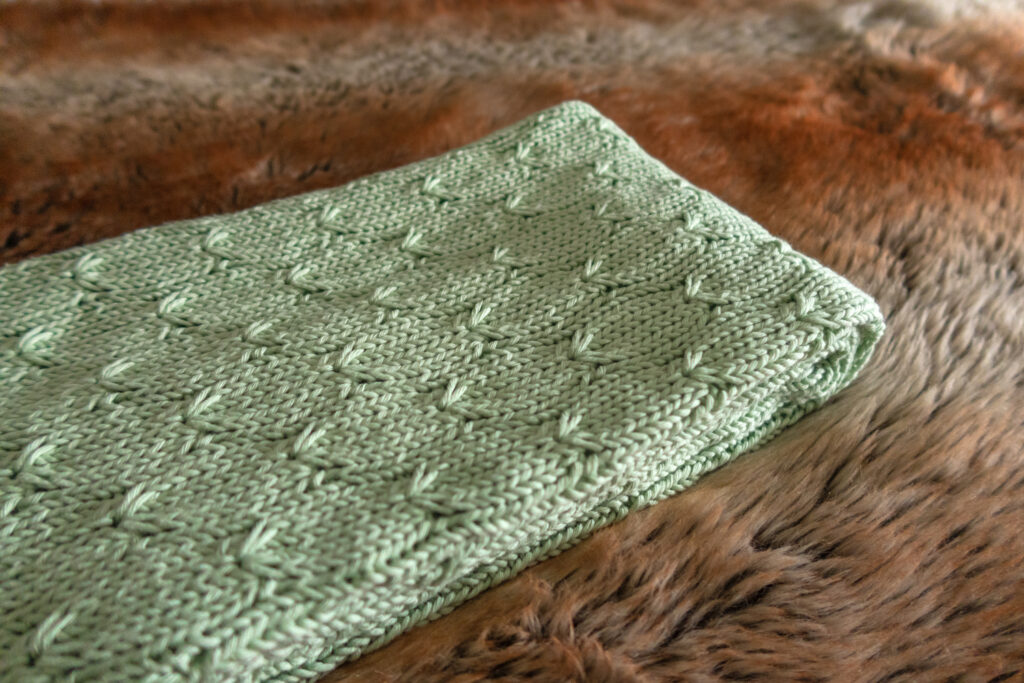 A green knitted baby blanket pattern